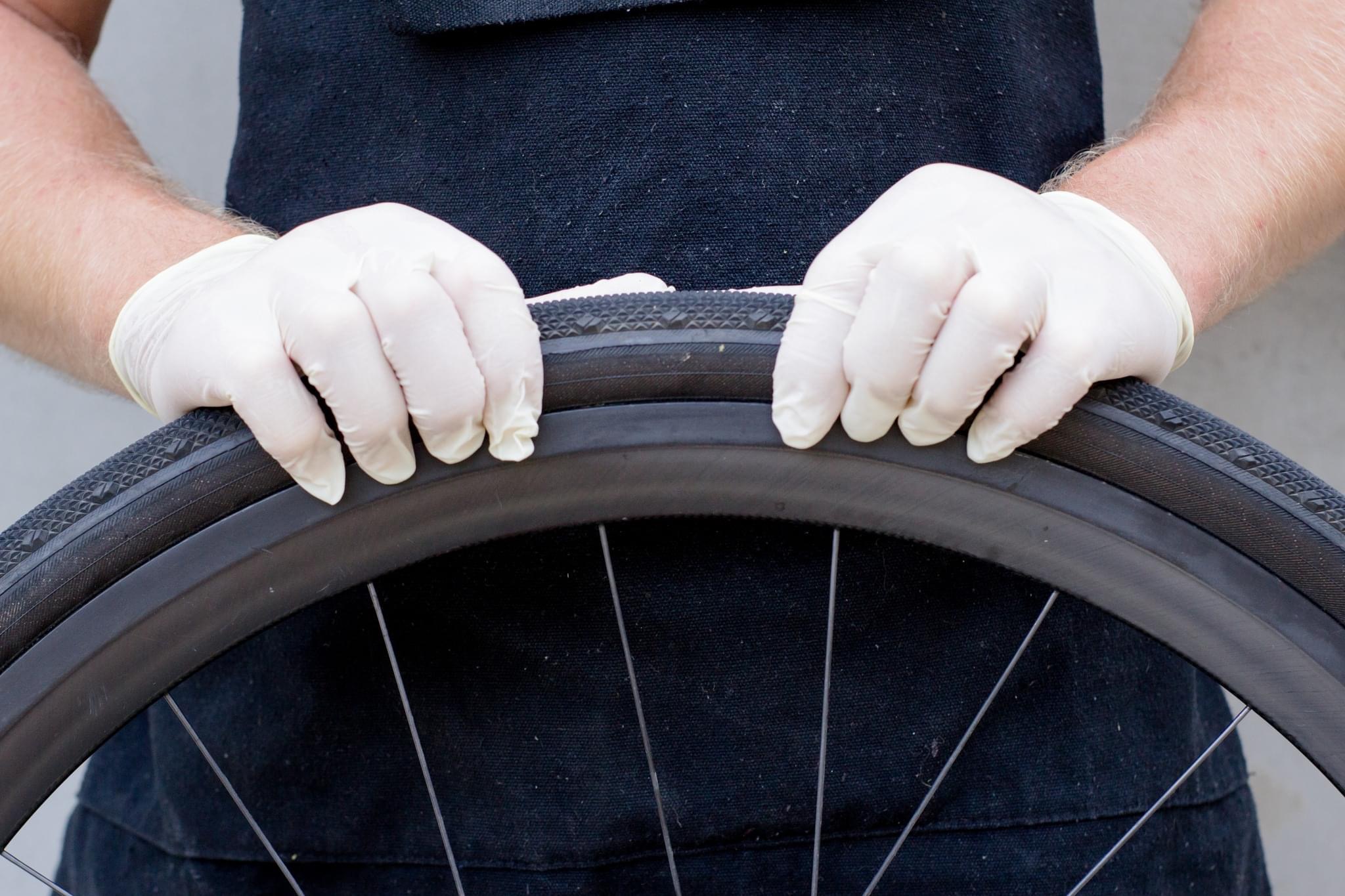 gloved hands grasp a tire on a bicycle wheel